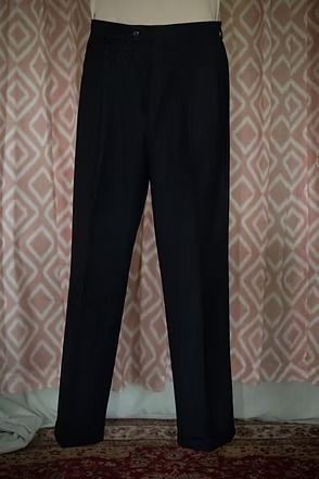 Black dress pants hanging against a patterned curtain.