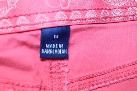 Red pants hanging on a hanger against a beige background.