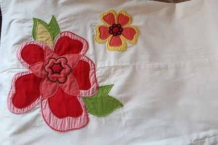 White fabric with two embroidered flowers: a large red flower and a smaller yellow-orange flower with green leaves.