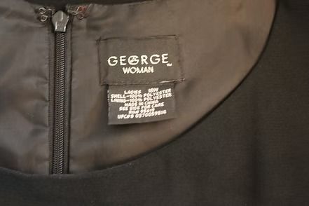 Close-up of a George Woman clothing label on a dark garment with a zipper.