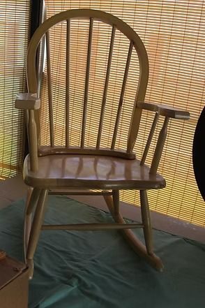 Wooden rocking chair with a brown cushioned seat, in front of a bamboo screen outdoors.
