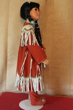 Native doll in red and white traditional dress with long black braids on a stand