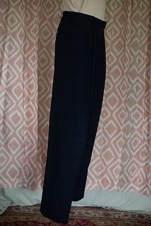 Black trousers hanging against a patterned curtain backdrop.