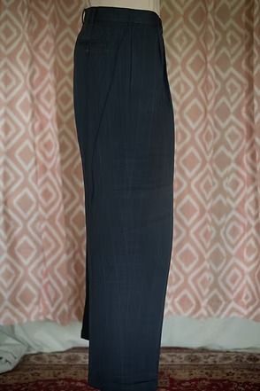 Dark navy trousers hanging against a patterned wall and carpeted floor.