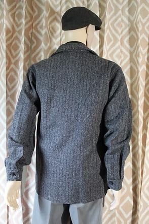 Mannequin wearing a dark cap and gray textured jacket against patterned curtains
