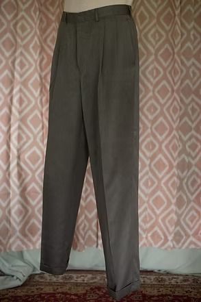 Dark gray pleated trousers hanging indoors against a patterned wall.