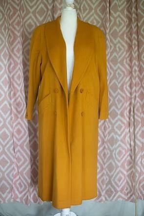 Mustard yellow long coat on a mannequin against a patterned curtain.