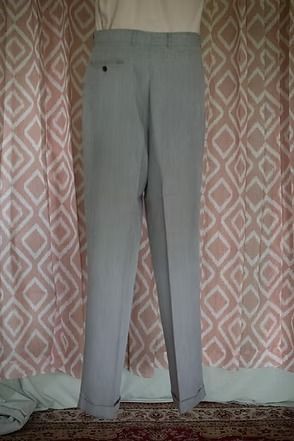 Light gray pants hanging against patterned curtains, with a small fabric item on the floor nearby