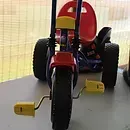 Red ride-on toy tractor with yellow wheels, viewed from the front indoors.
