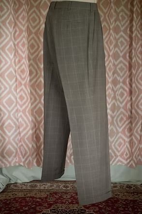 Gray plaid dress pants hanging in front of a pink patterned curtain and carpeted floor