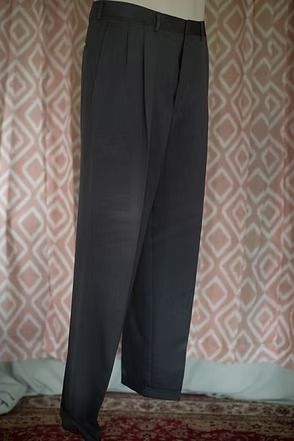 Black pleated trousers hanging against a patterned pink curtain
