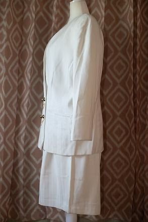 White suit jacket and skirt displayed on a mannequin against a patterned brown backdrop