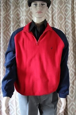 Mannequin wearing a red and navy pullover with gray pants in front of patterned curtains
