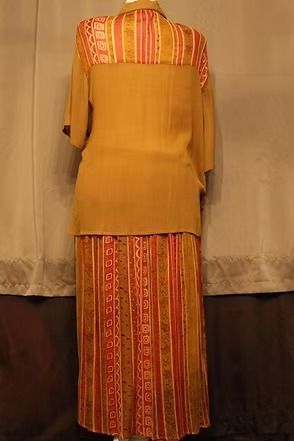 Mannequin wearing a mustard top and striped orange skirt against a tan backdrop