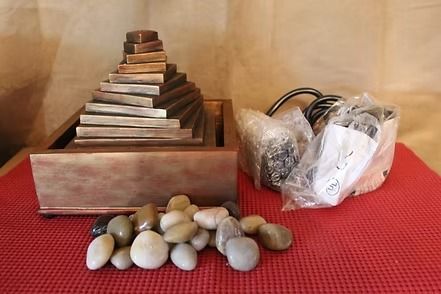 Metal staircase model on wooden base beside bubble wrap and small stones on a red mat