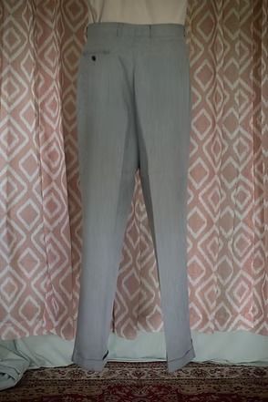 Light gray pants hanging against patterned curtains, with a small fabric item on the floor nearby