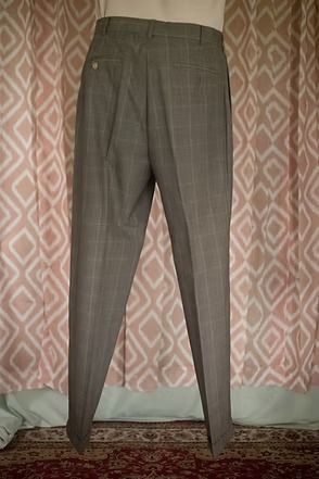 Gray plaid dress pants hanging in front of a pink patterned curtain and carpeted floor