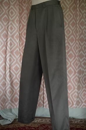Dark gray pleated trousers hanging indoors against a patterned wall.