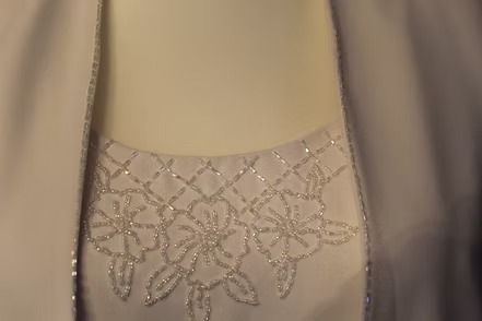 White ceremonial robe with wide sleeves and decorative hem, displayed on a mannequin against a dark background