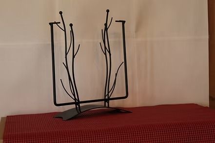White flower in glass vase on metal stand atop a red checkered tablecloth.