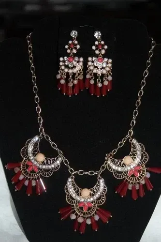 Red and silver jewelry set with matching necklace and earrings on a black display stand