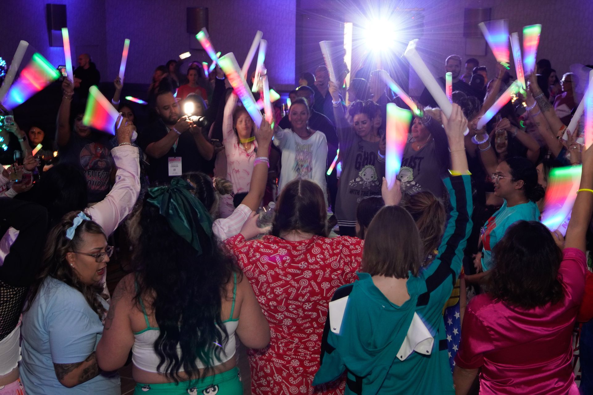 A group of people are holding glow sticks in the air at a party.