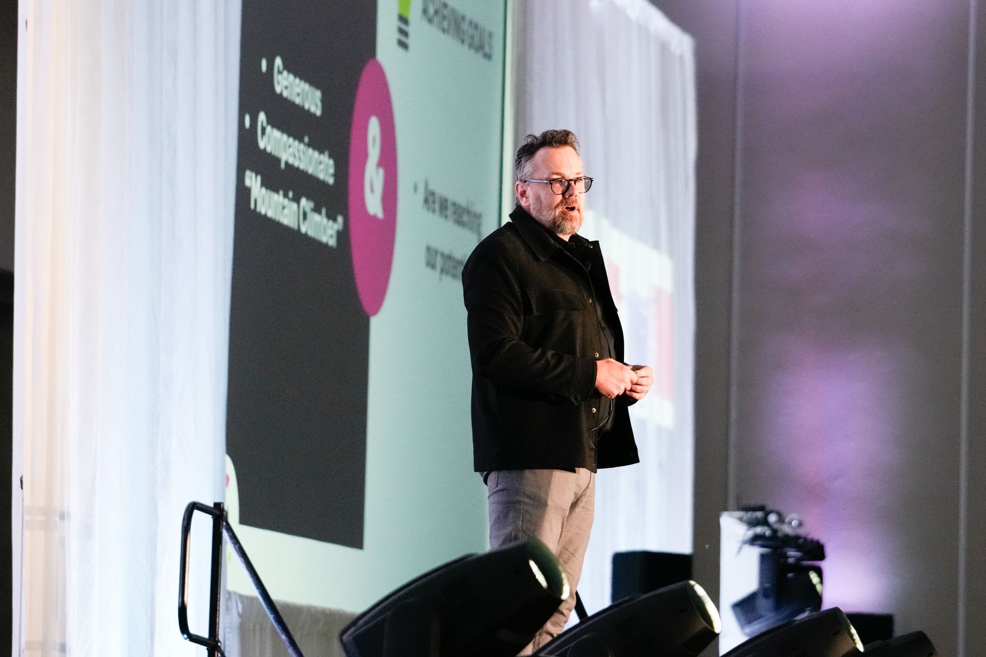 A man is standing in front of a large screen giving a presentation.