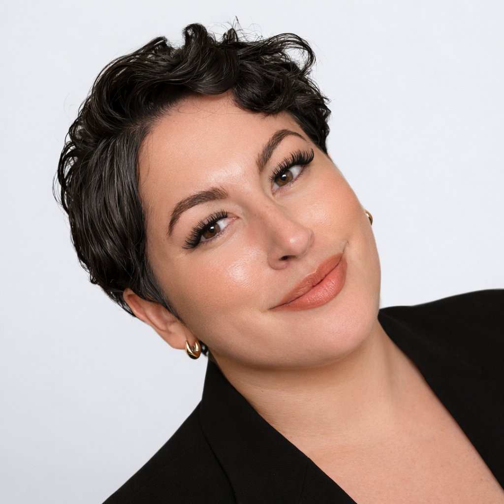 Portrait of a smiling person with short dark hair, wearing a black blazer against a light background
