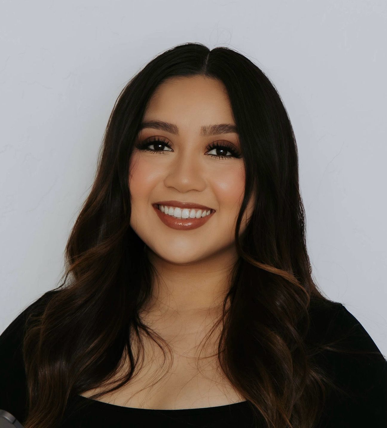 Portrait of a smiling woman with long dark hair against a light gray background
