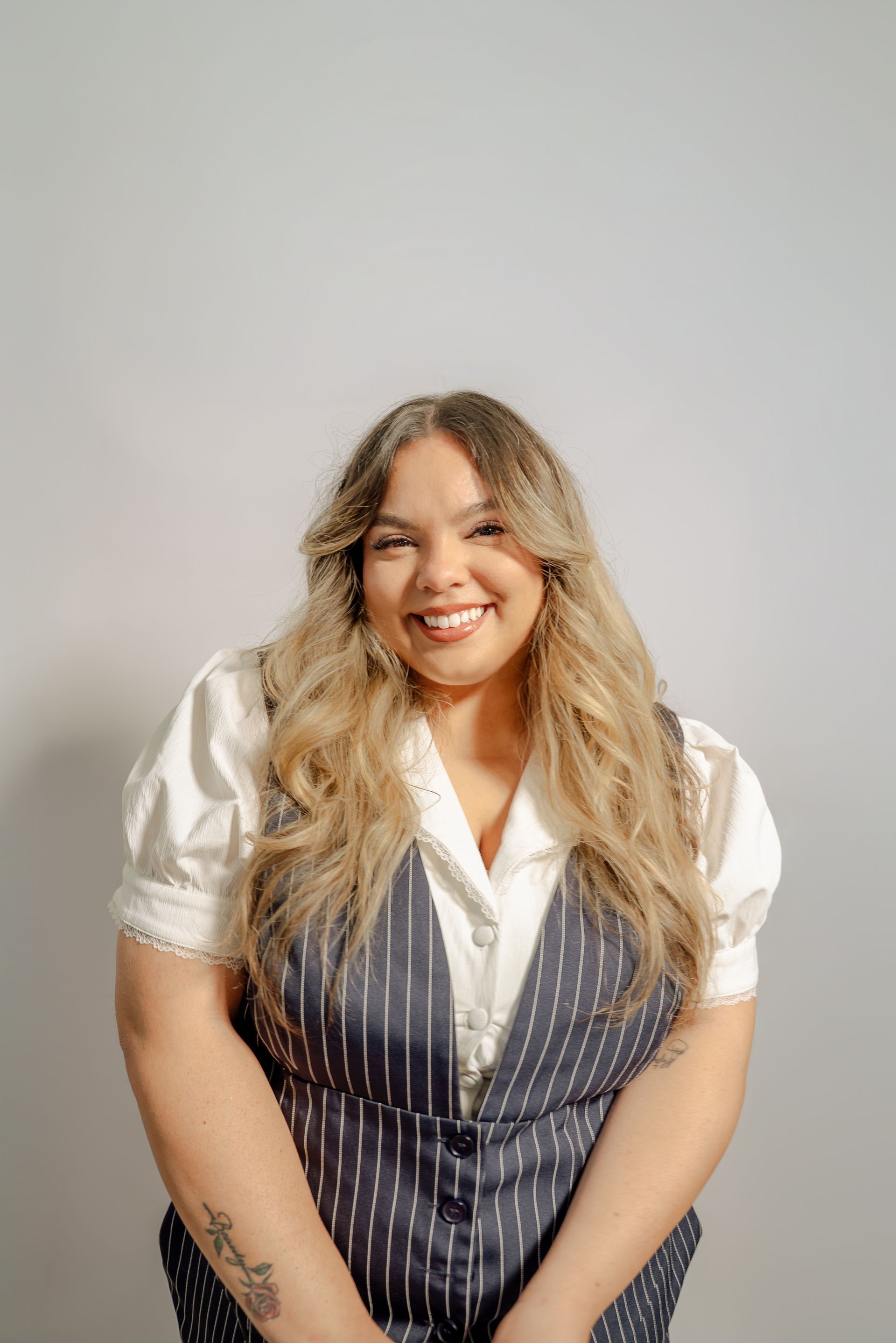 Smiling person in a white blouse and navy pinstripe vest against a plain gray background