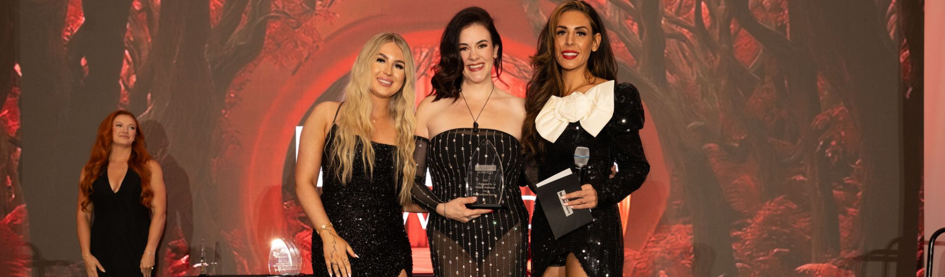 Three women in black stage outfits standing before a red fiery backdrop