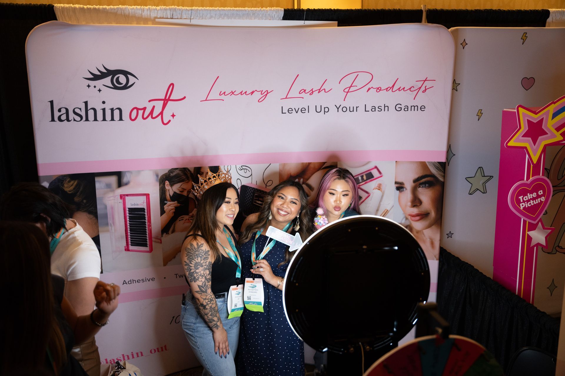 Two women are posing for a picture in front of a sign that says lash out.
