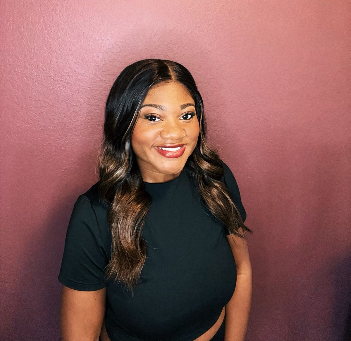 Smiling woman in a black top against a pink wall