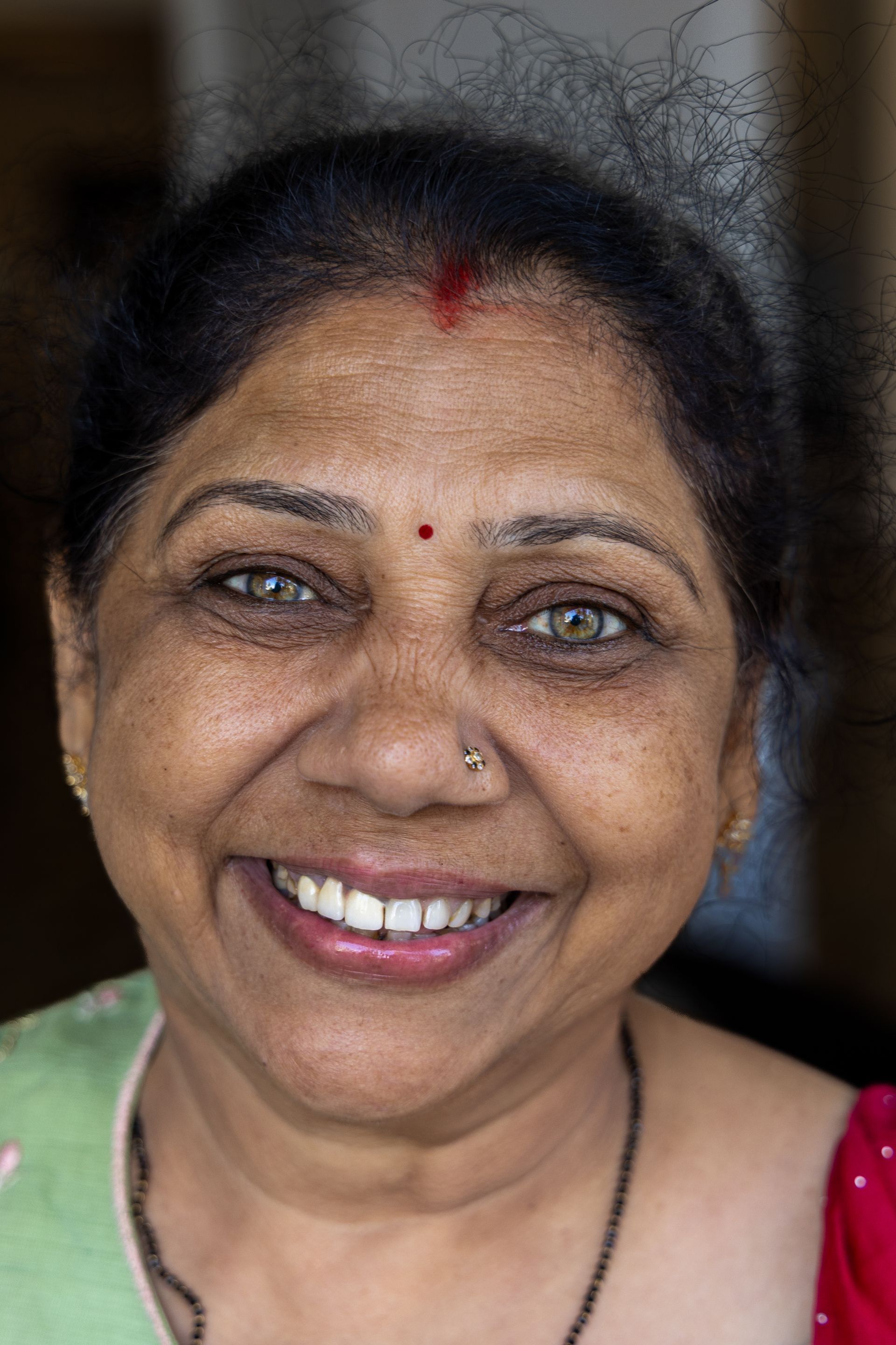 Lachende vrouw met een rode bindi en neusring, gekleed in een groen-rood topje.