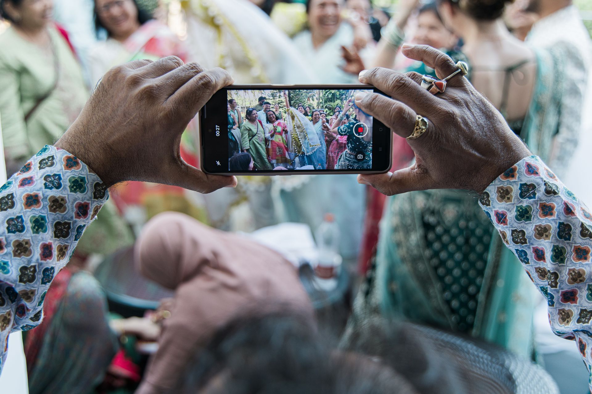 Handen die een smartphone vasthouden om een kleurrijk feestgedruis buiten vast te leggen