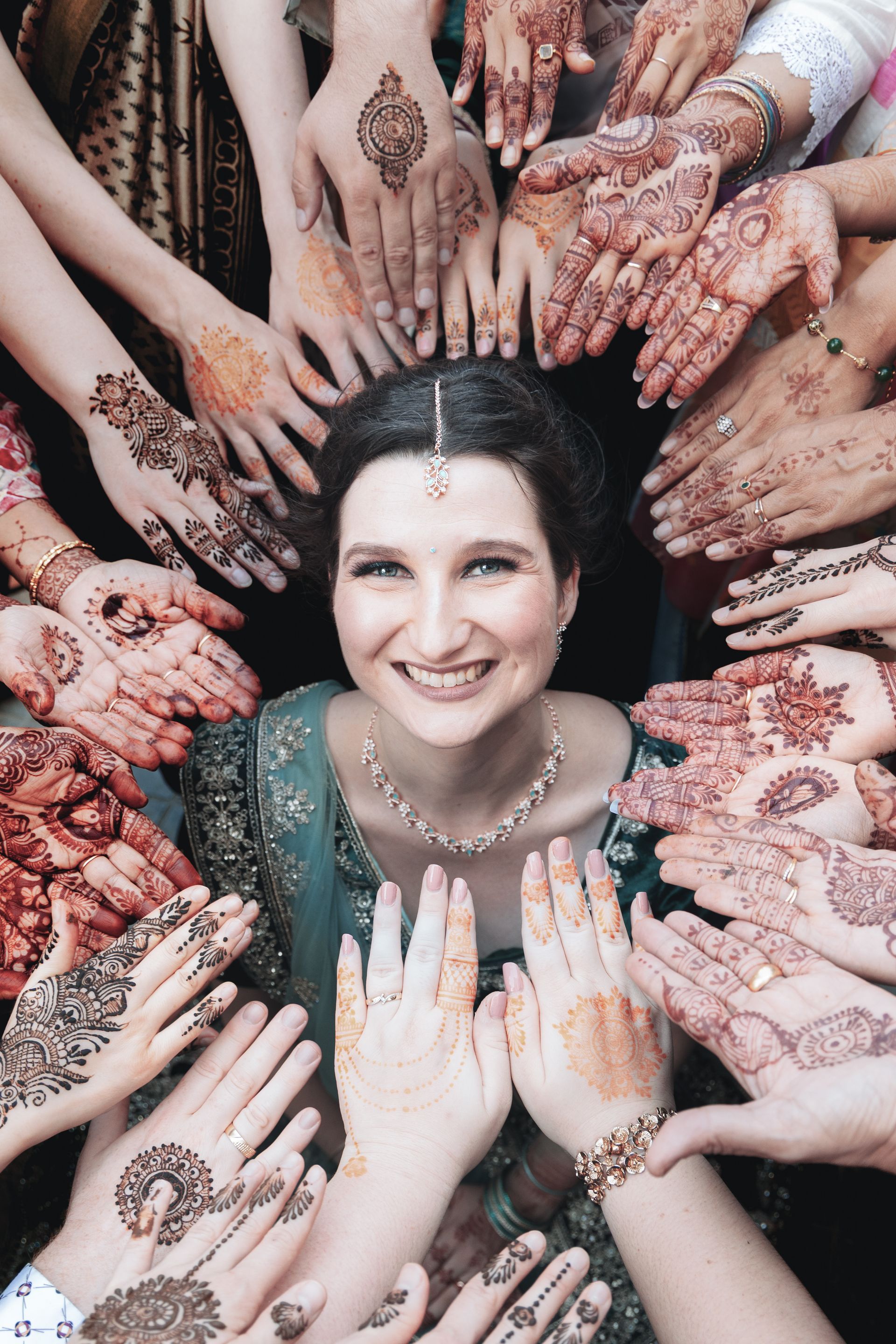 Een lachende vrouw omringd door vele met henna versierde handen in een feestelijke kring.