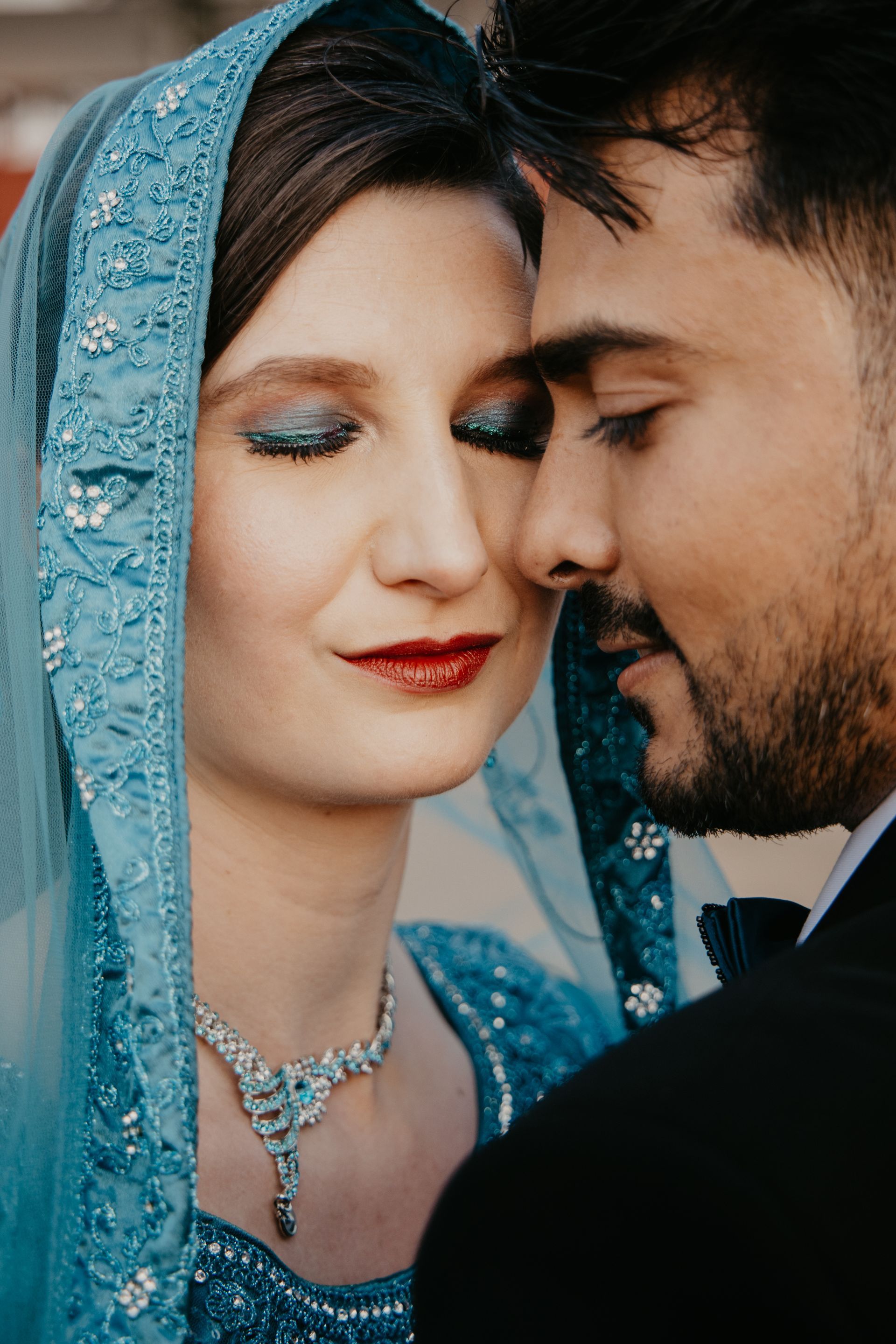 Twee mensen in blauwe traditionele kleding leunen dicht tegen elkaar aan met gesloten ogen en delen een intiem moment.