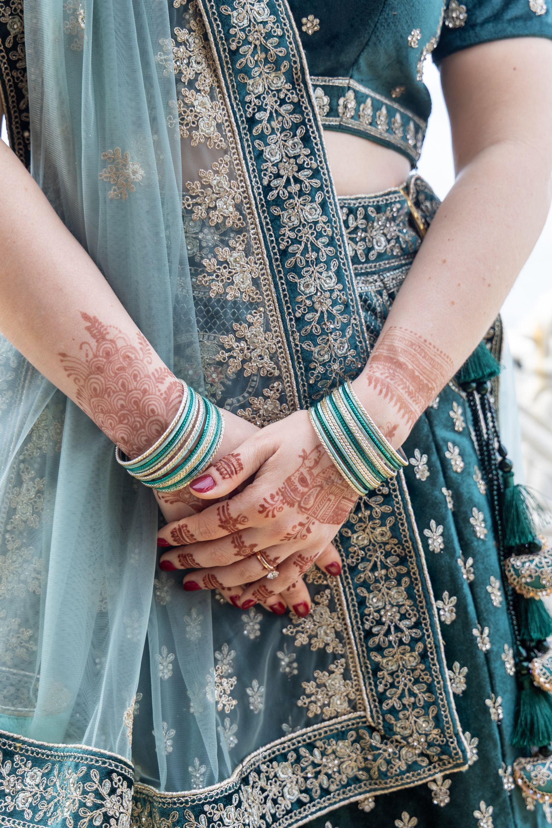 Bruid in een turquoise geborduurde outfit met dupatta, handen gevouwen, met groene armbanden en hennaversieringen.