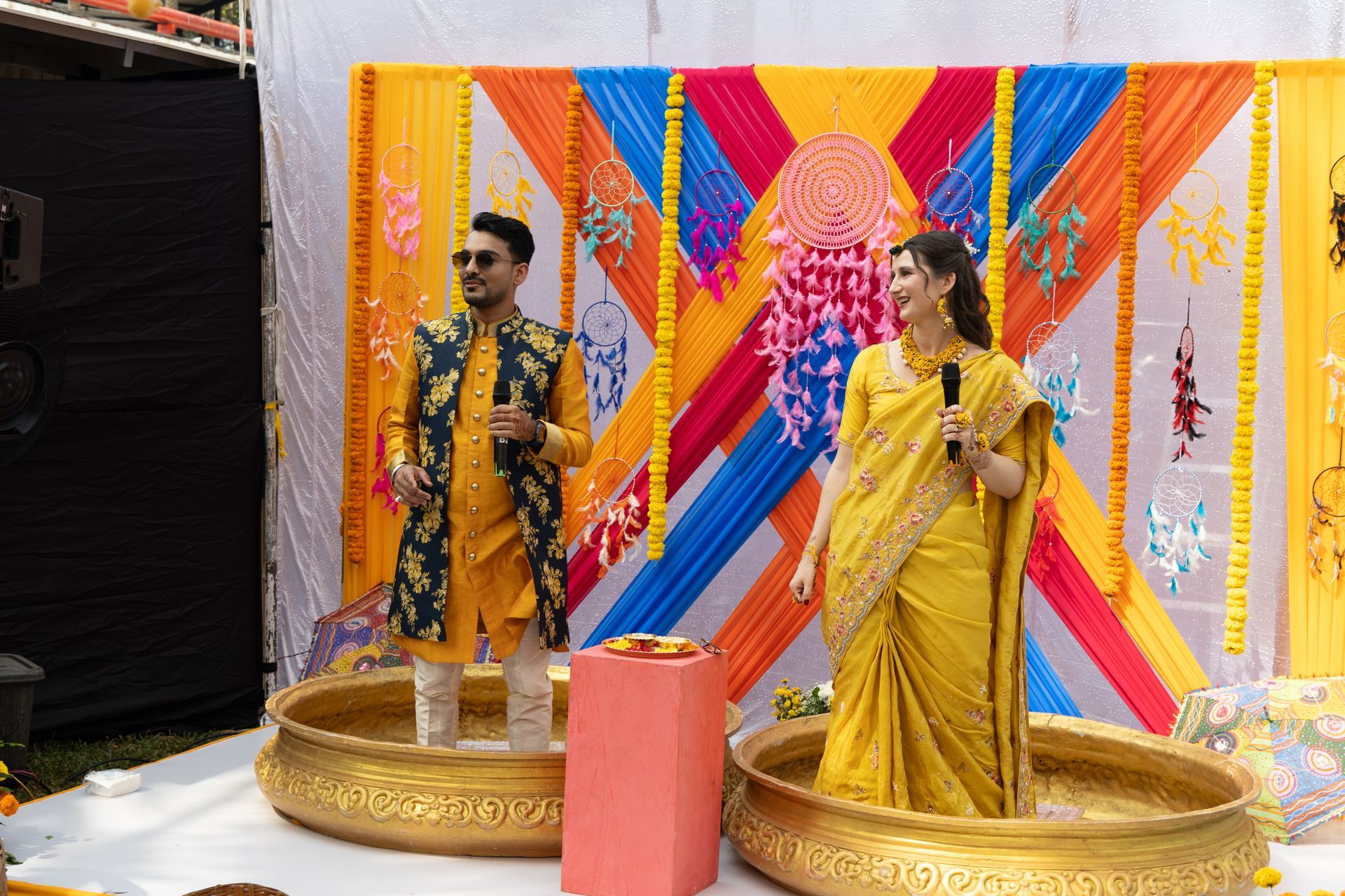Mannequins in traditionele gele kleding op gouden sokkels voor een kleurrijke geometrische achtergrond.