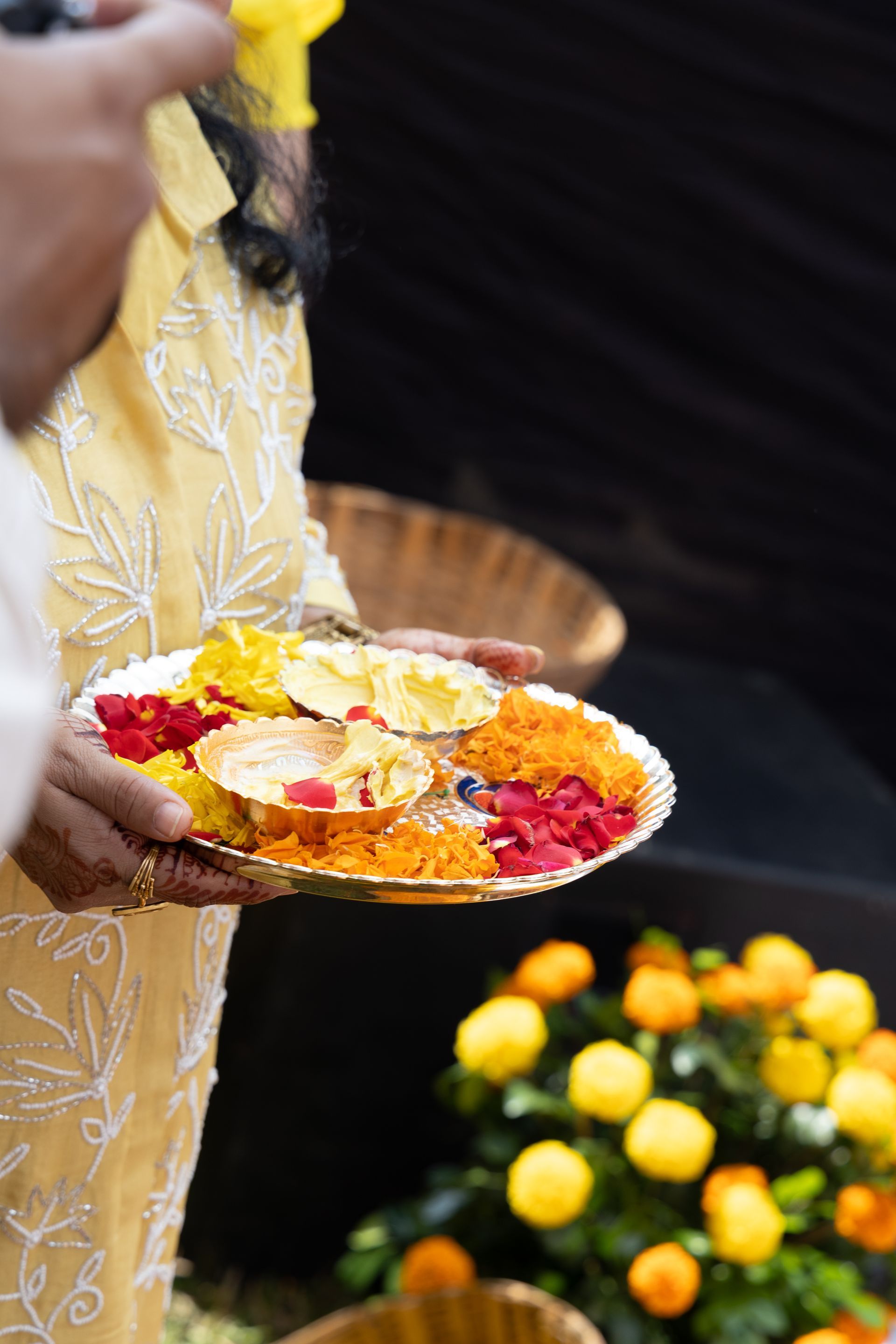 Een persoon houdt een versierde schaal met bloemen en offergaven vast tijdens een rituele ceremonie in de buitenlucht.