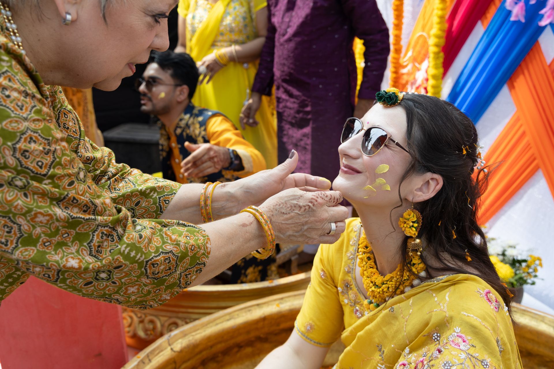Vrouw in gele sari ontvangt een ceremoniële gezichtsbehandeling tijdens een feestelijke bijeenkomst.
