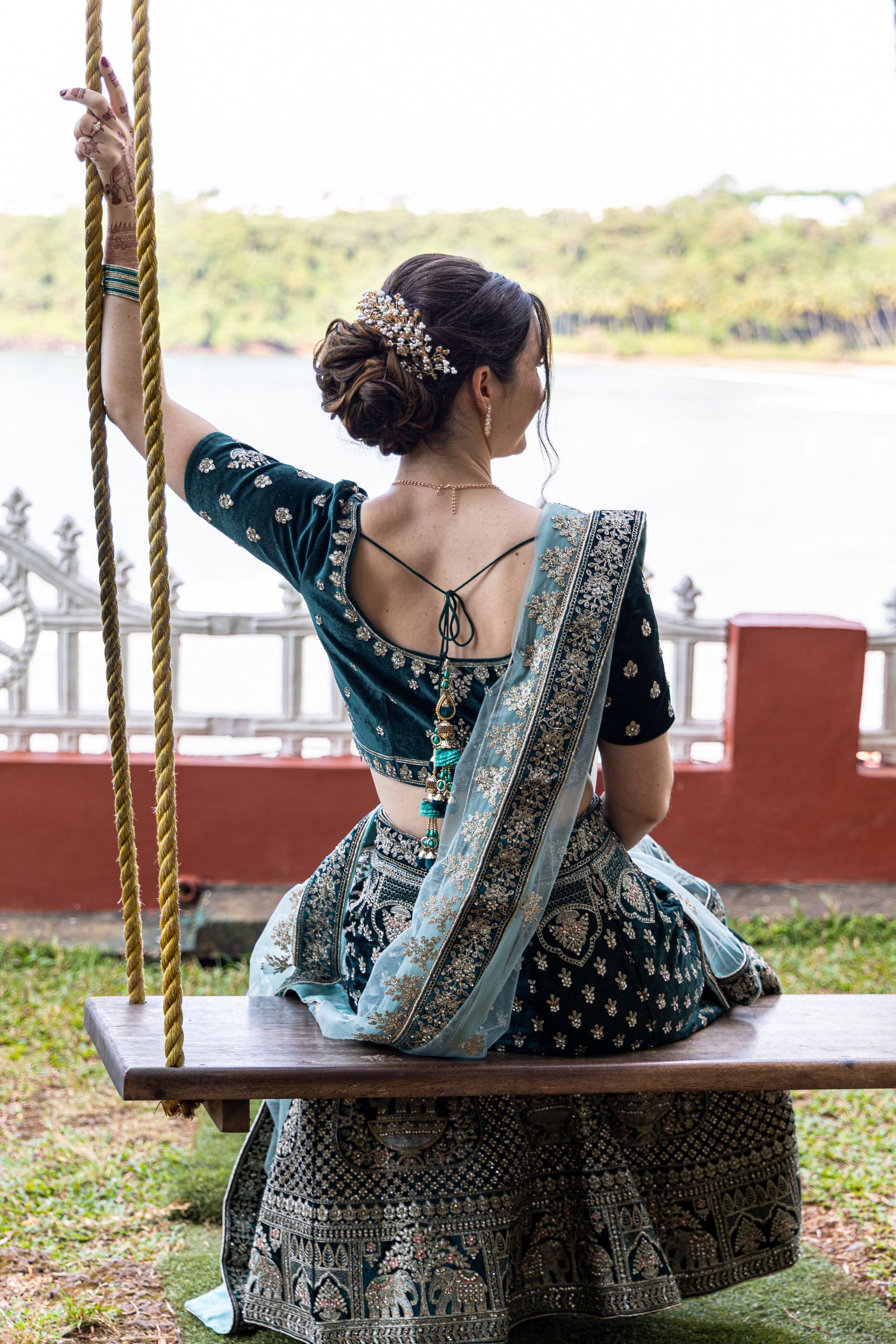 Vrouw in een turquoise sari zittend op een schommel, van achteren gezien, bij een terras aan het meer.