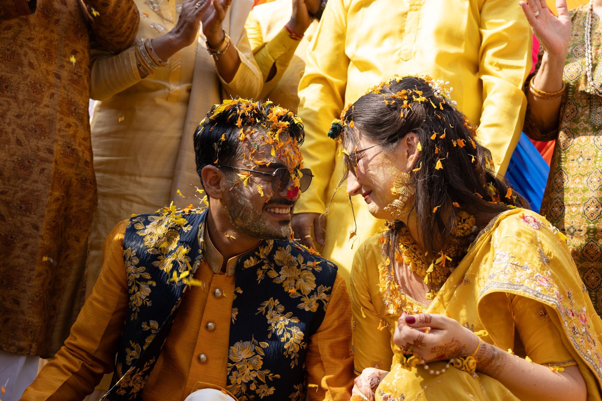 Twee mensen in gele kleding glimlachen tijdens een feestelijke bijeenkomst, bedekt met bloemblaadjes.