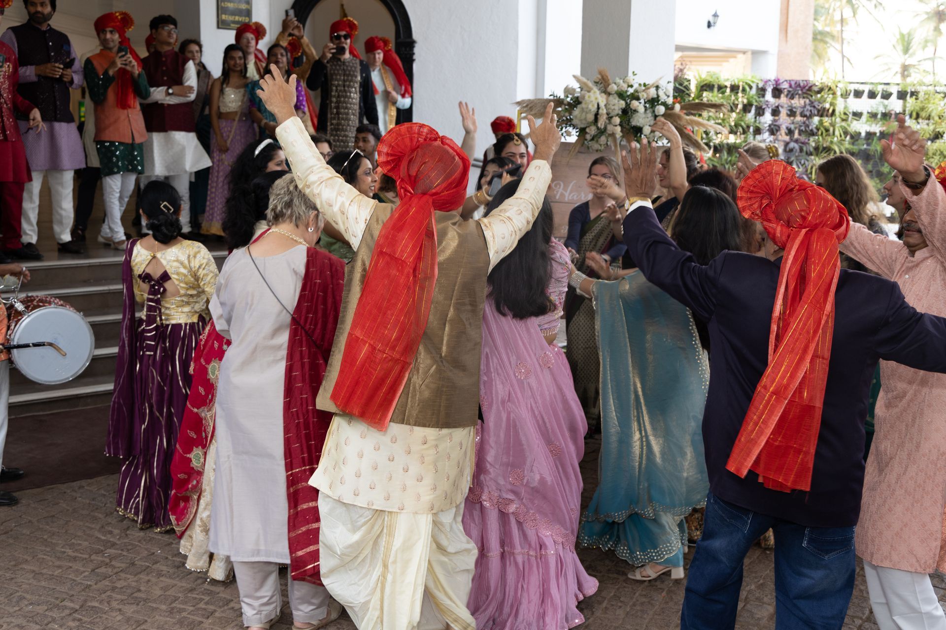 Dansers in kleurrijke traditionele kleding voeren hun dans uit met opgeheven armen tijdens een feestelijke binnenviering.