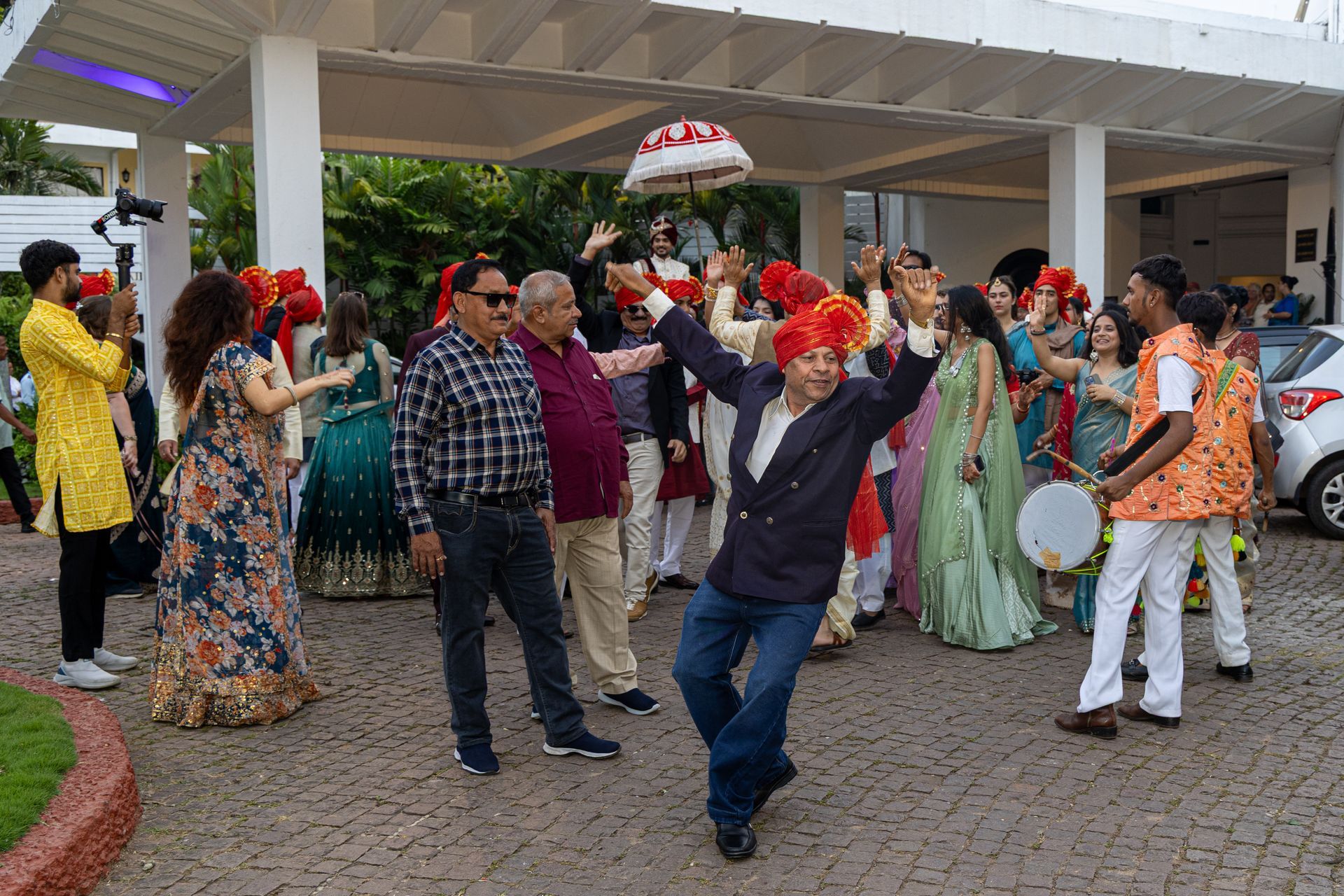 Mensen dansen vrolijk in kleurrijke kleding tijdens een openluchtfeest onder een afdak.