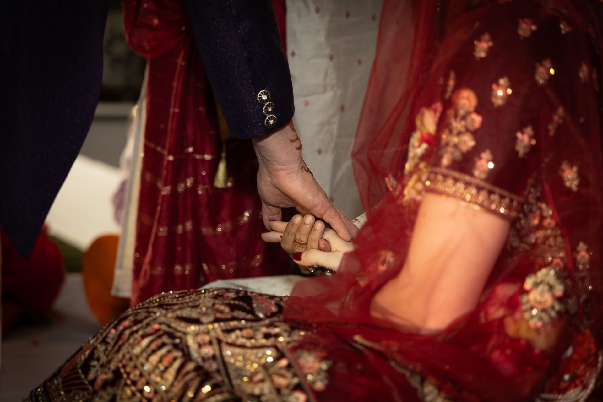 Bruid en bruidegom hand in hand tijdens een huwelijksceremonie, gekleed in traditionele rode en gouden kleding.