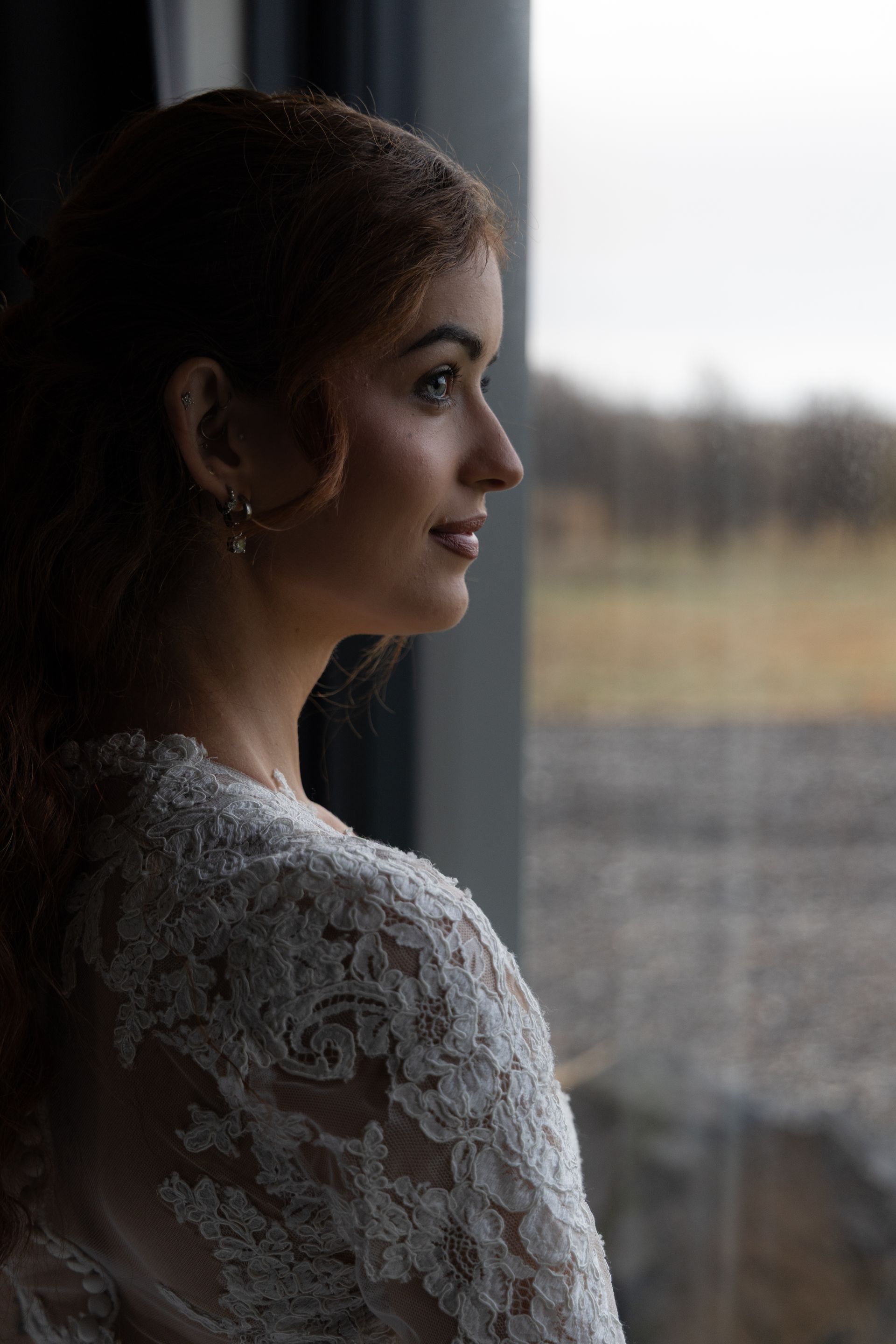 Een vrouw in een witte kanten top kijkt uit het raam naar een wazig buitenlandschap.