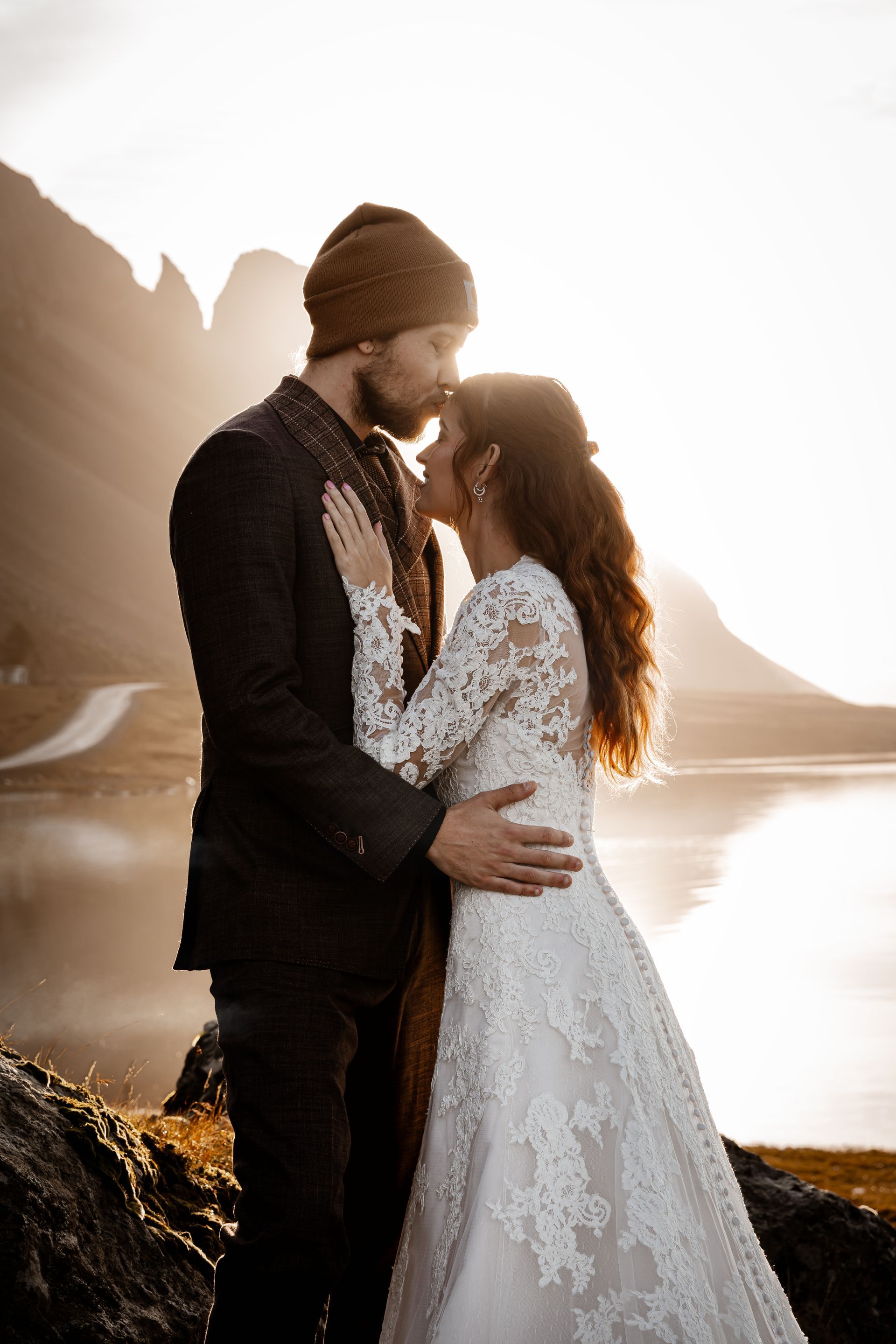Een stel dat elkaar omhelst bij zonsondergang aan het meer, met op de achtergrond de bergen en het water die prachtig glinsteren.