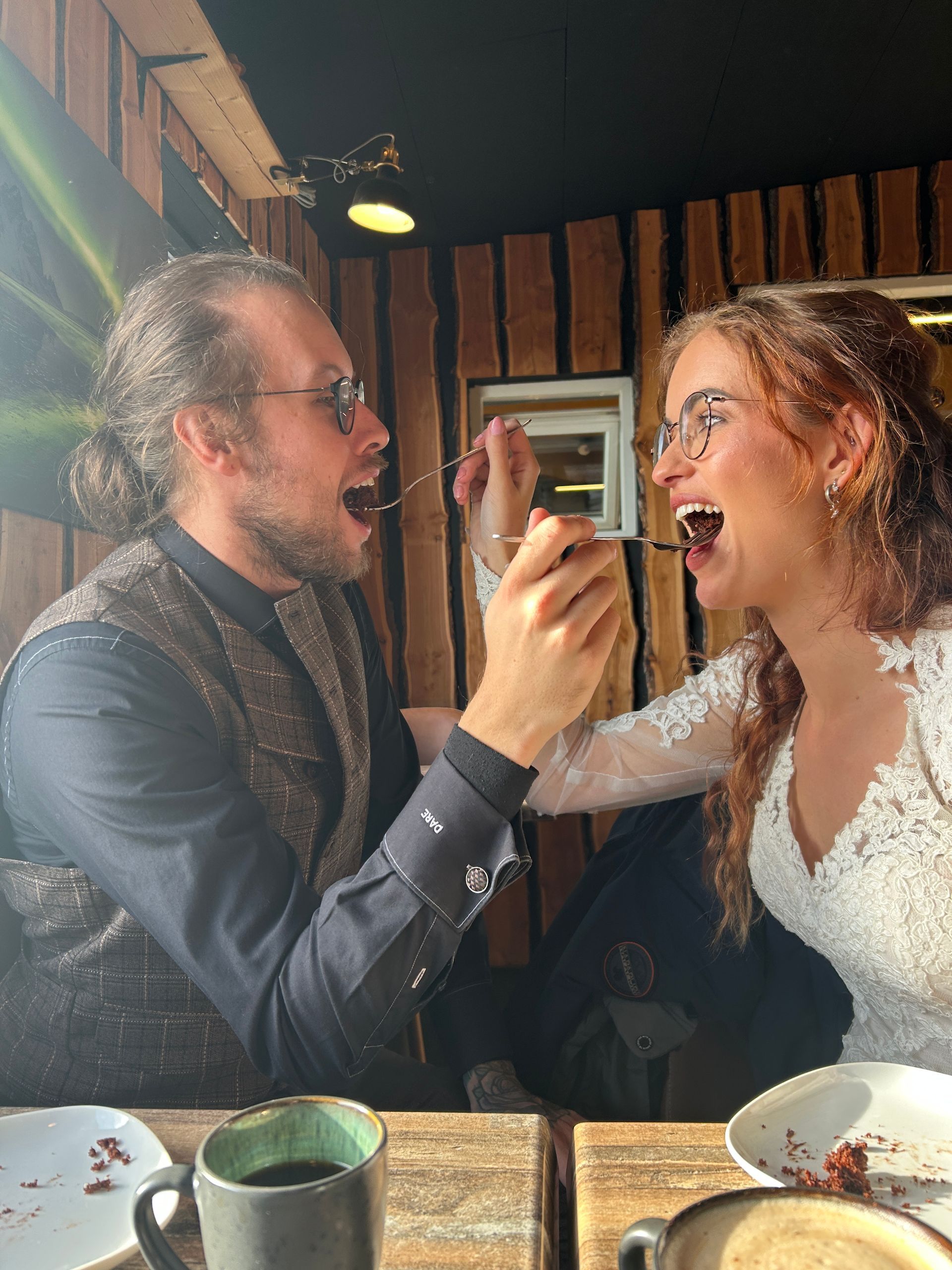 Twee mensen glimlachen en voeren elkaar dessert aan een restauranttafel.