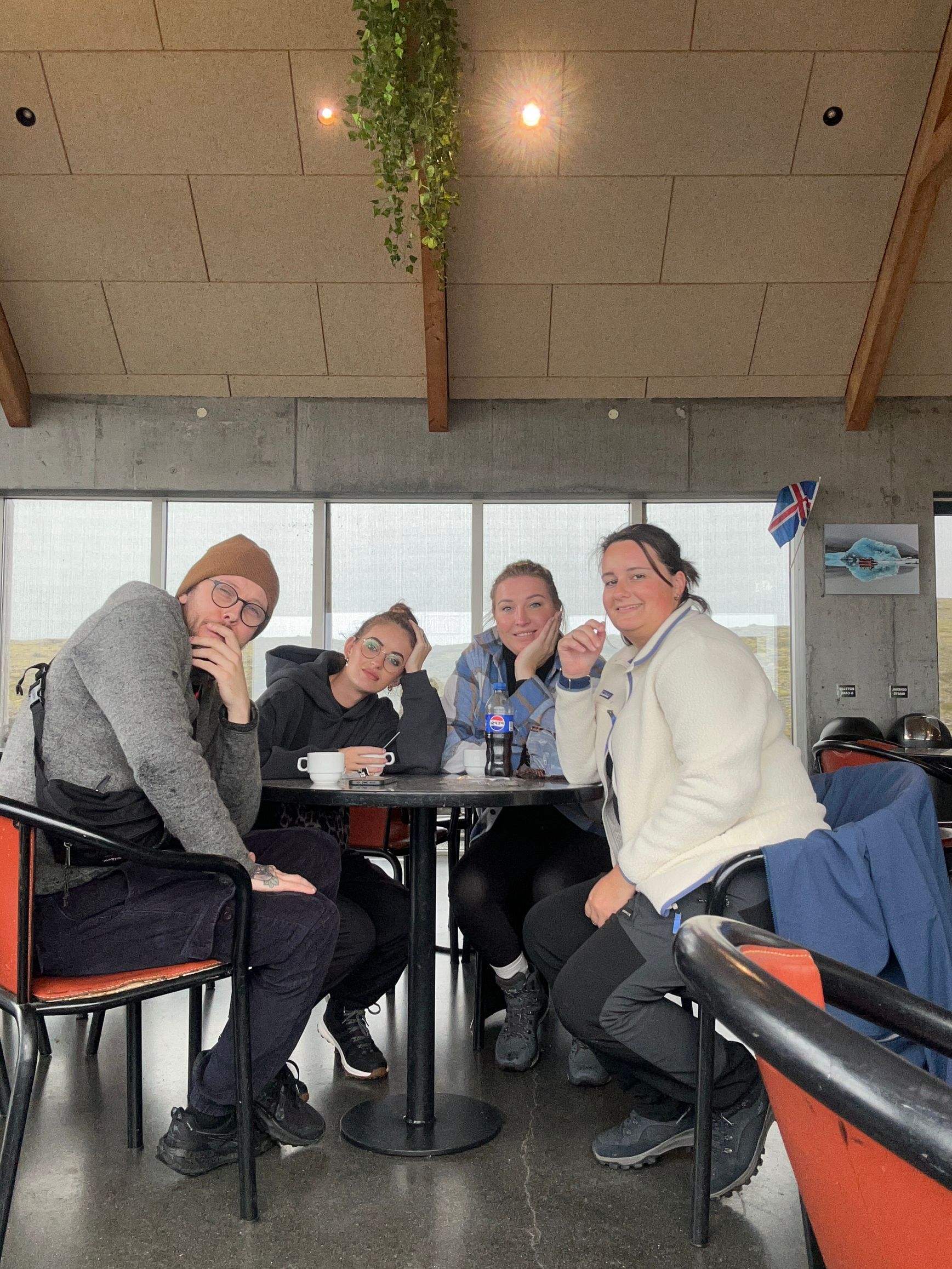 Vier vrienden zitten rond een cafétafel, lachend en pratend in een lichte, overdekte lounge.
